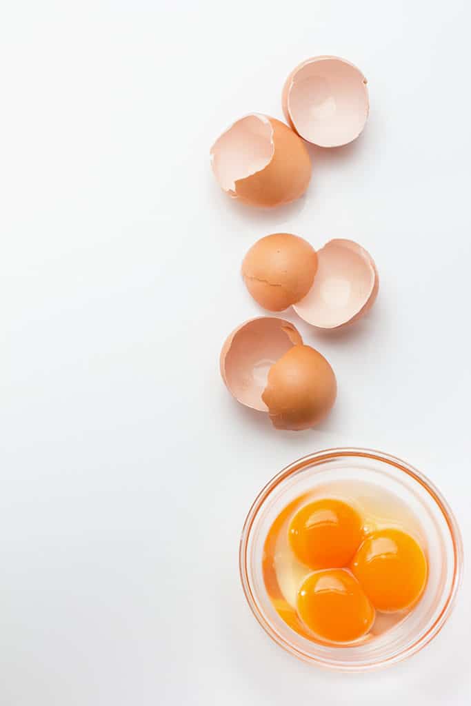 Broken eggshells with egg yolks in glass bowl