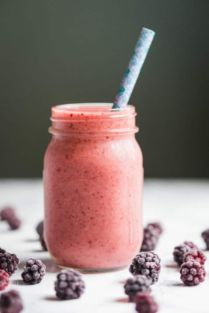a berry kombucha smoothie in a mason jar with a blue straw