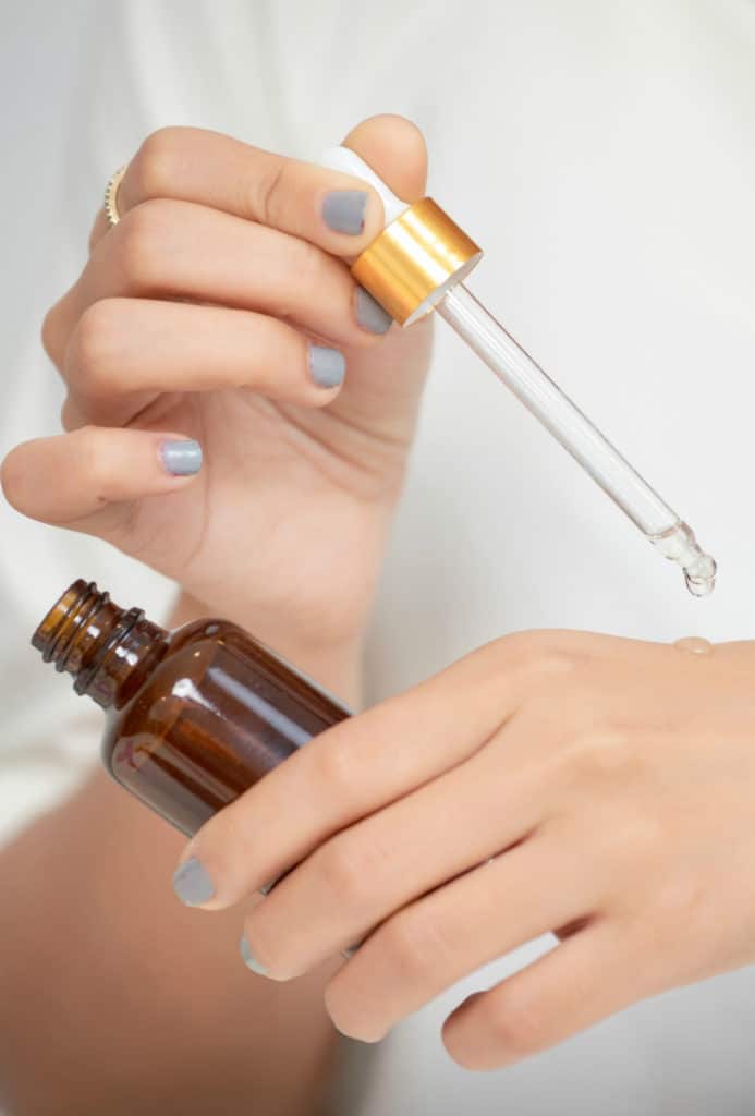 A woman applying serum from a dropper bottle onto her hand