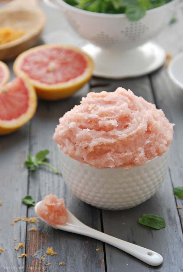 light pink grapefruit sugar scrub in a white bowl with a white spoon on the table