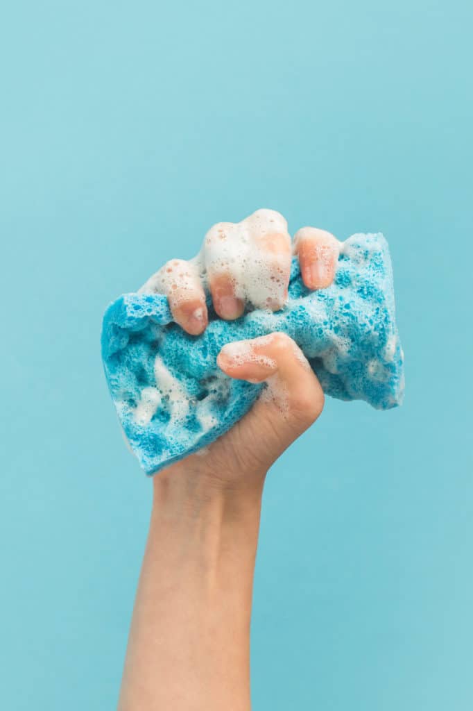 A hand squeezing a soapy blue sponge
