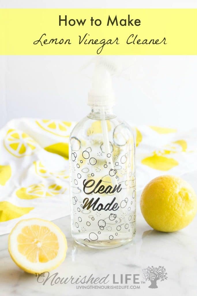A glass spray bottle of lemon vinegar cleaner next to lemon halves on a marble counter