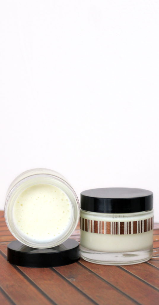small jars of rosacea cream with black lids on wooden table