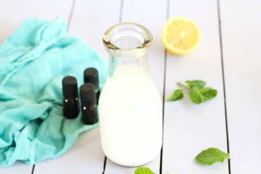 A glass bottle of homemade mouthwash on a table with herbs and essential oils