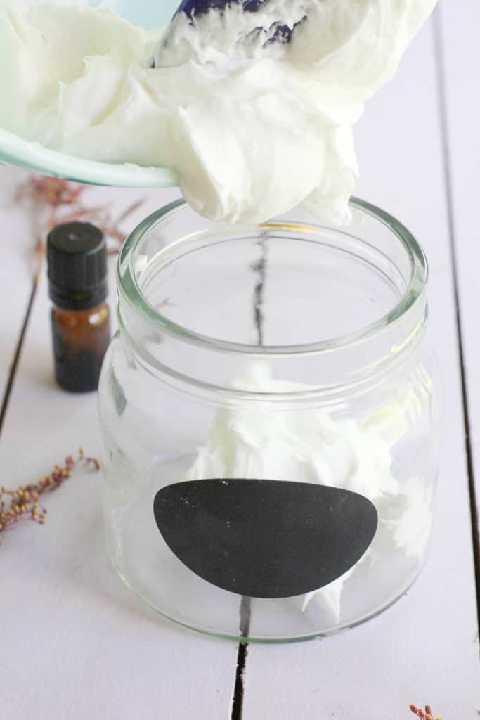 Spooning fluffy whipped coconut oil body butter into a glass jar