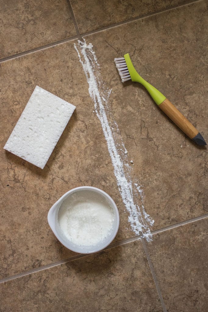 DIY grout cleaner in a bowl with a sponge and cleaning brush on stone tiles