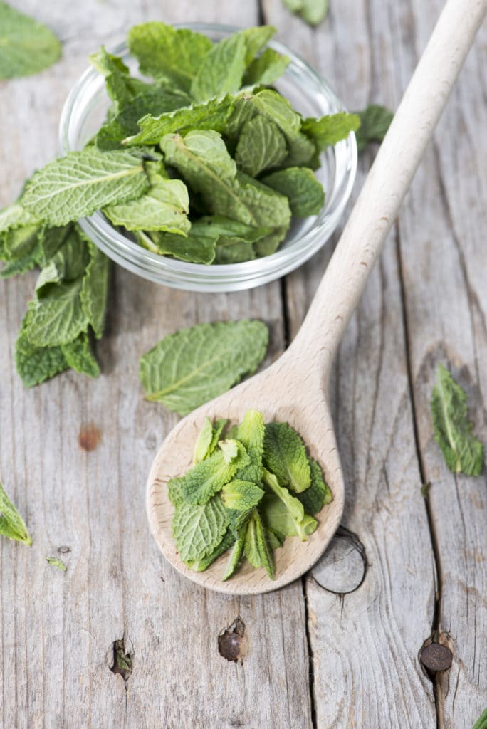 Freshly cut mint leaves in a wooden spoon on a rustic table