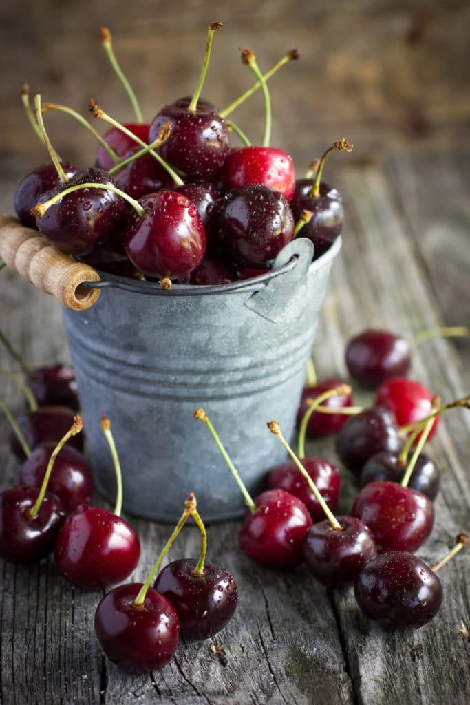 Cherries in a small bucket on a rustic table